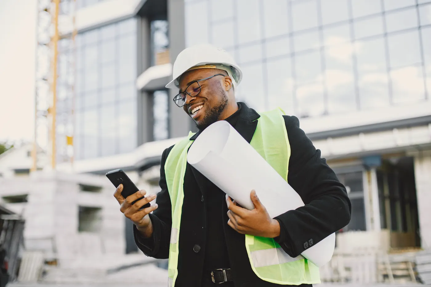 Young black man with blueprint standing near glass building