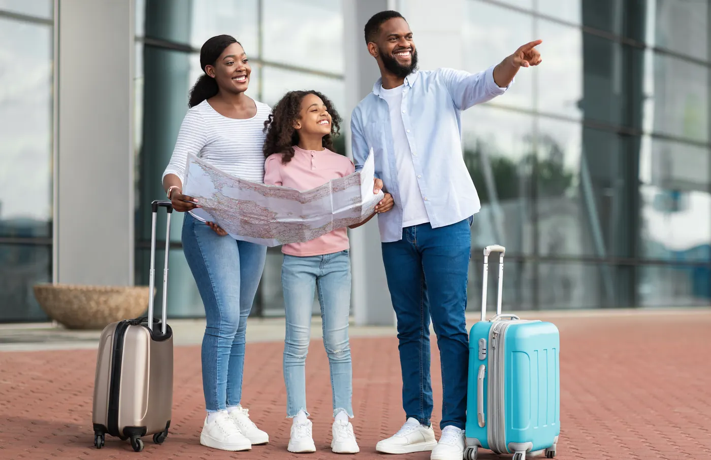 Young Black family with suitcases holding a city map outside an airport
