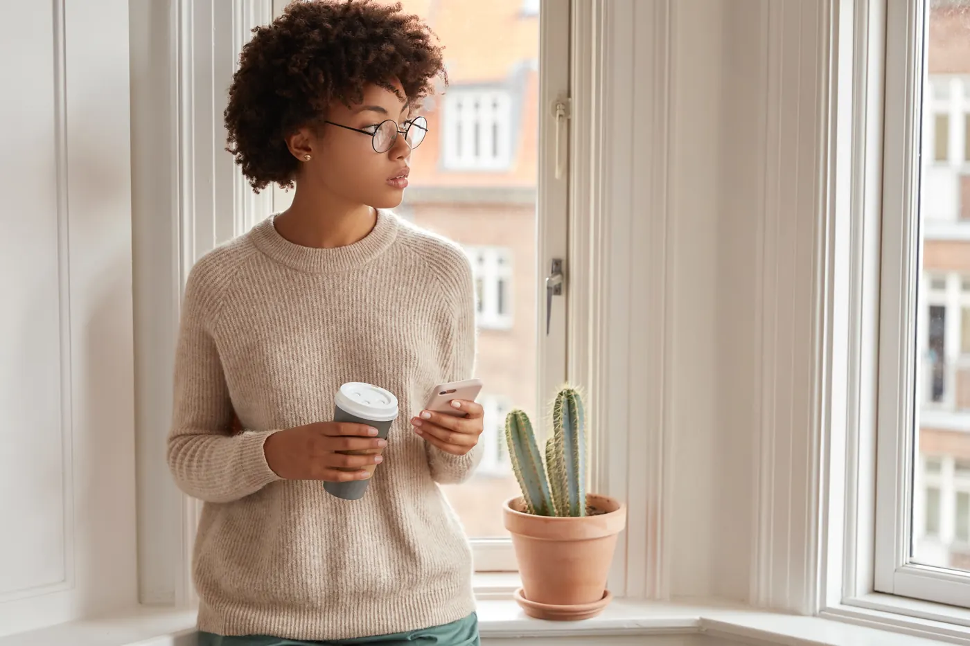 Indoor shot of thoughtful dark skinned woman uses smart phone for online communication