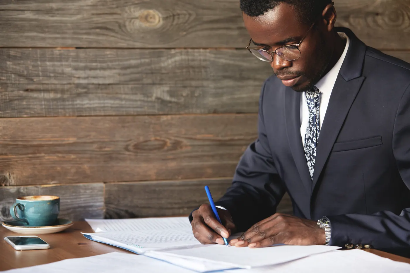 Serious black corporate worker in formal suit and spectacles signing a lucrative contract