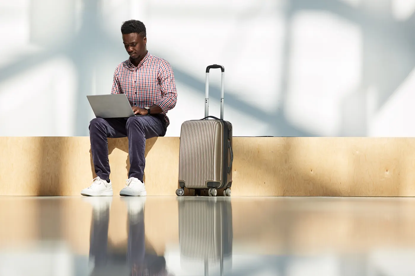 African young businessman sitting at the airport with luggage working on laptop